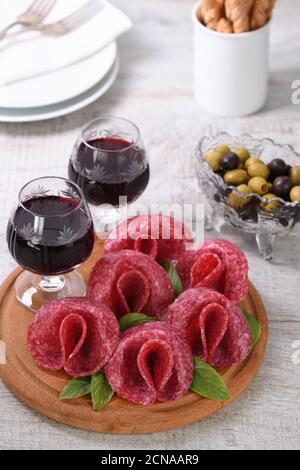 Leichte Mahlzeit Snack aus Salami gefaltet in Form einer Blume mit einem Glas Sherry auf einer Holzschale. Cl Stockfoto