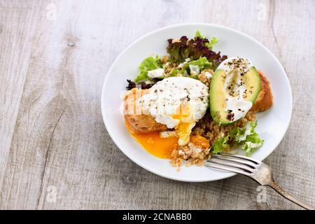 Ein gesunder und ausgewogener Frühstücksteller. Benedict's Ei breitet sich auf einem gerösteten Toast mit einem halben avoca aus Stockfoto