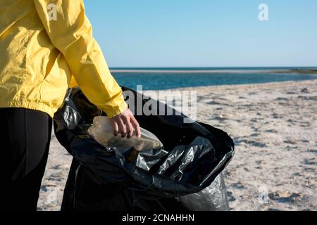 Frau nimmt Müll und Kunststoffe auf und säubert den Strand mit einer Mülltüte. Umweltaktivisten gegen den Klimawandel und die Umweltverschmutzung o Stockfoto