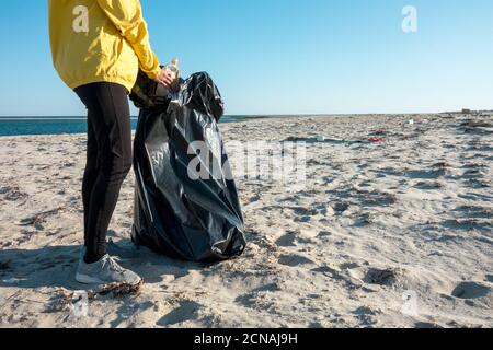 Frau nimmt Müll und Kunststoffe auf und säubert den Strand mit einer Mülltüte. Umweltaktivisten gegen den Klimawandel und die Umweltverschmutzung o Stockfoto