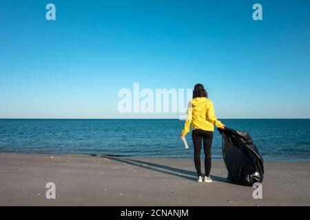 Frau nimmt Müll und Kunststoffe auf und säubert den Strand mit einer Mülltüte. Umweltaktivisten gegen den Klimawandel und die Umweltverschmutzung o Stockfoto