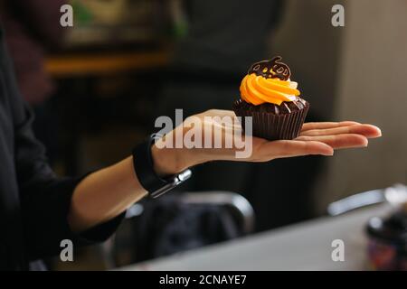 Leckere Schokolade Cupcake mit Orangencreme, verziert mit Schokolade Kürbis in der Hand eines Mädchens. Süßigkeiten für die Feier von Halloween. Stockfoto