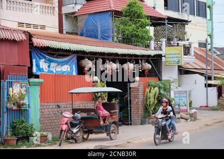 Kambodscha, Siem Reap 12/08/2018 ein kleines asiatisches Mädchen spielt in einer Motorrikscha, ein Roller fährt die Straße entlang Stockfoto