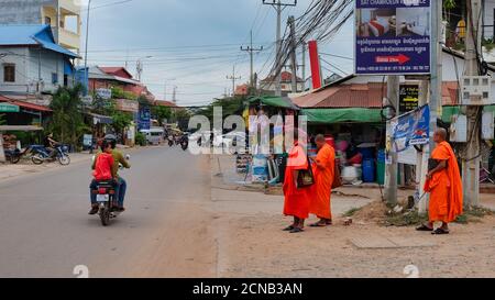 Kambodscha, Siem Reap 08/12/2018 mehrere buddhistische Mönche in orangefarbenen Kleidern stehen am Straßenrand, mehrere Motorroller fahren entlang der Straße Stockfoto