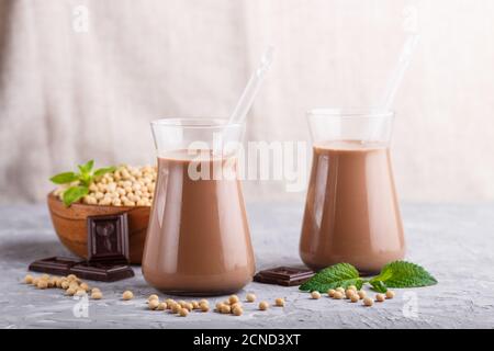 Bio-Soja-Schokoladenmilch aus nicht-Milchprodukten in Glas und Holzplatte mit Sojabohnen auf grauem Betongrund. Vegan gesundes Lebensmittelkonzept, Nahaufnahme, Seite Stockfoto