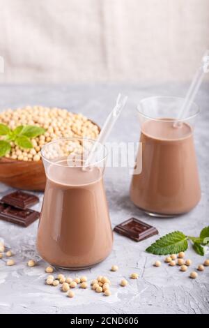 Bio-Soja-Schokoladenmilch aus nicht-Milchprodukten in Glas und Holzplatte mit Sojabohnen auf grauem Betongrund. Vegan gesundes Lebensmittelkonzept, Nahaufnahme, Seite Stockfoto