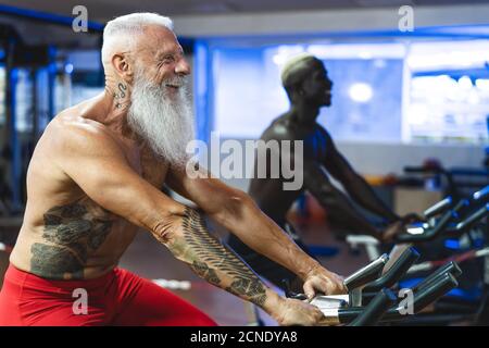Ältere und junge Männer machen Fahrrad-Übungen im Fitnessstudio - Menschen mit unterschiedlichem Alter und Renntraining auf Radfahrmaschine Im Wellness-Center Stockfoto