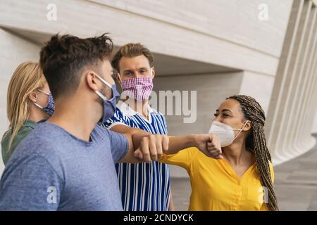 Junge Freunde tragen Gesicht Schutzmaske tun neue soziale Distanzierung Begrüßen Sie mit Ellenbogen Beulen zur Verhinderung Corona-Virus Ausbreitung Stockfoto