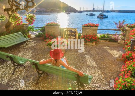 Elegante Frau in rot mit Hut in Marciana Marina Waterfront, dem blumigen alten Viertel Borgo al Cotone, Insel Elba, Toskanischer Archipel Stockfoto