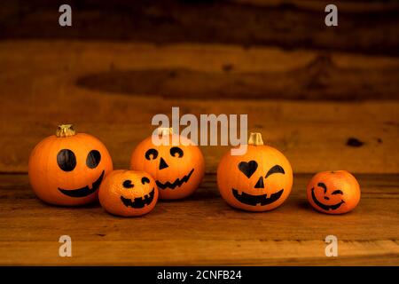 Kleine Kürbisse und Mandarinen mit bemalten Gesichtern für Halloween an Holzhintergrund Stockfoto