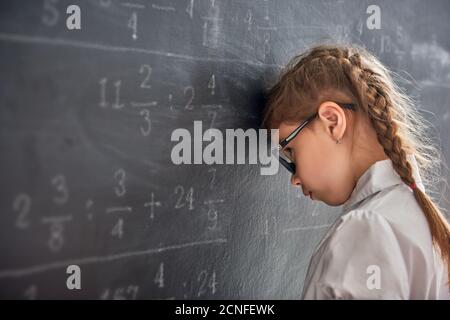 Harter Schultag! Trauriges Kind in der Nähe der Tafel drinnen. Kind lernt in der Klasse. Komplexe Mathematik, Arithmetik und Beispiele. Zahlen geschrieben mit chal Stockfoto