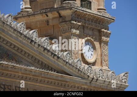 Nahaufnahme Detail der Uhr Gesicht auf dem Turm der Kirche der Himmelfahrt, Mosta auch bekannt als die Rotunde. Zeigt das Dach und die Turmspitze. Stockfoto
