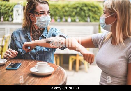 Junge Freundinnen stoßen ihre Ellbogen, anstatt mit zu grüßen Eine Umarmung - Vermeiden Sie die Ausbreitung von Coronavirus tragen schützende Masken - Soziale Distanz Konz Stockfoto