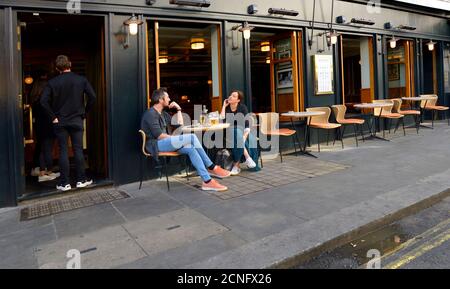 London, England, Großbritannien. Menschen, die allein vor einer Bar in Soho während der COVID-Pandemie im September 2020 sitzen Stockfoto