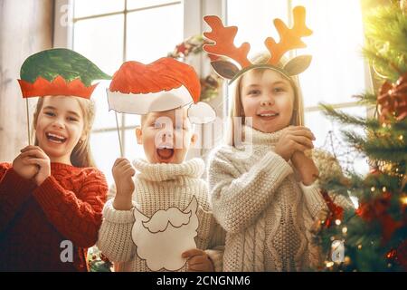 Frohe Weihnachten und schöne Feiertage! Kinder mit Papierzubehör für Foto: Weihnachtsmütze, Geweih eines Rentiers und der Elfenkopf. Familienfest. Stockfoto