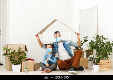 Familie in medizinischen Masken im Gesicht schaut auf die Kamera, während sie im Zimmer zu Hause steht. Stockfoto