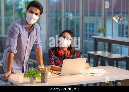 Schöne asiatische Frau und kaukasischen Mann trägt medizinische Hygiene zu schützen Mask tun Arbeit zusammen im Wohnzimmer mit Laptop-Computern In orangefarbenem Licht Stockfoto