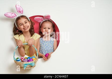 Nette kleine Kinder tragen Hasenohren am Ostertag. Mädchen mit bemalten Eiern auf weißem und rosa Hintergrund. Stockfoto