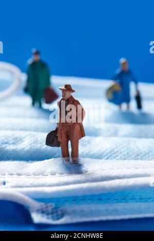 Einige Miniatur-Menschen auf einer blauen Einweg-Gesichtsmaske, die Konzepte wie zurück zur Arbeit oder Reisen während der covid-19 Pandemie Stockfoto