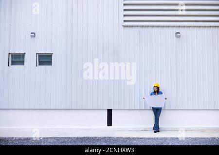 Schöne asiatische weibliche Ingenieur in Jeans Kleid trägt gelbe Sicherheit Hut Arbeit auf Baustelle außerhalb Büro. Idee für modernes Arbeiten w Stockfoto