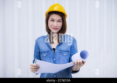 Schöne asiatische weibliche Ingenieur in Jeans Kleid trägt gelbe Sicherheit Hut Arbeit auf Baustelle außerhalb Büro. Idee für modernes Arbeiten w Stockfoto