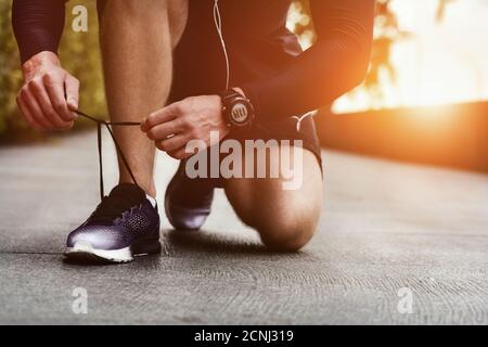 Nahaufnahme von Sportlern, die Sneakers binden. Nicht erkennbarer Mann hält Schnürschuh im Freien. Sportschuhe Konzept. Stockfoto
