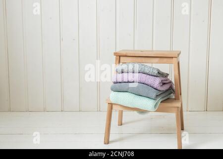 Stapel von gemütlichen Strickpullover auf einer Holzleiter. Skandinavischer Stil. Weiße Holzwand Stockfoto