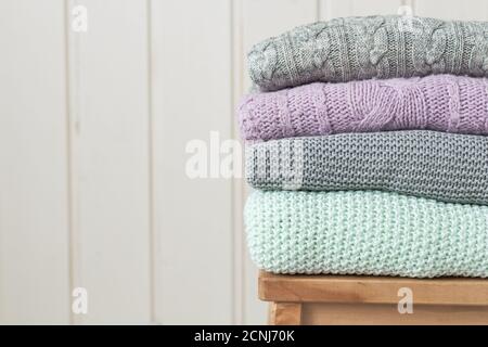 Stapel von kuschelig gestrickten Kleidern auf einer Holzleiter. Skandinavischer Stil. Weiße Holzwand Stockfoto