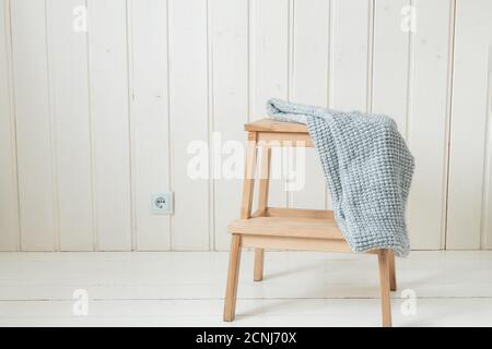Kuscheliger Strickschal auf einer Holzleiter. Skandinavischer Stil. Weiße Holzwand Stockfoto