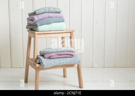 Stapel von gemütlichen Strickpullover auf einer Holzleiter. Skandinavischer Stil. Weiße Holzwand Stockfoto