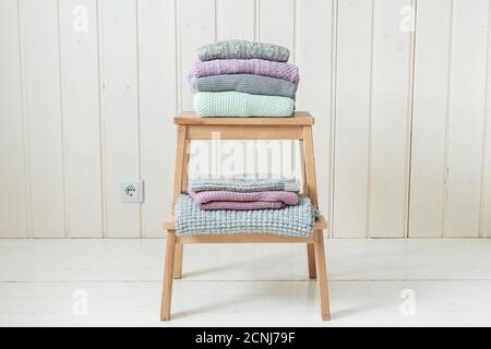 Stapel von kuschelig gestrickten Kleidern auf einer Holzleiter. Skandinavischer Stil. Weiße Holzwand Stockfoto