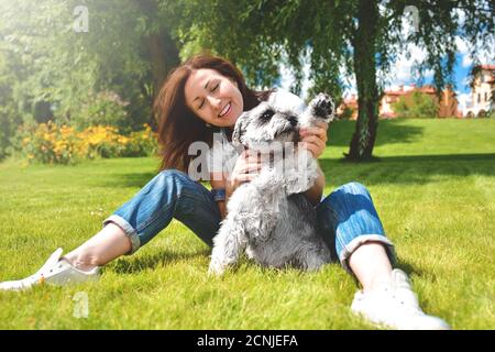 Hübsche Erwachsene kaukasische glückliche Frau, die sich an einem sonnigen Tag mit ihrem geliebten Hund im Park ausruhte. Weibchen liegt auf dem Gras, lächelnd an Stockfoto