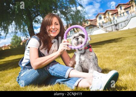 Kaukasische fröhliche Frau spielt mit ihrem geliebten Hund im Park. Das Konzept der Liebe zu Tieren. Beste Freunde. Hunderasse Schnau Stockfoto