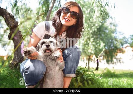Glückliche kaukasische Frau in Sonnenbrillen Ruhe in der Natur mit ihrem geliebten Hund schnauzer. Konzept der Liebe zu Tieren. Beste Freunde Stockfoto