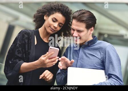Geschäftstreffen. Mann und Frau diskutieren über die Arbeit und schauen auf den Smartphone-Bildschirm. Gemeinsam im Freien arbeiten. Stockfoto