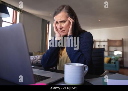 Besorgt kaukasische Frau, die Zeit zu Hause, soziale Distanzierung und Selbstisolierung in Quarantäne Lockdown, sitzen am Tisch, mit einem Laptop, massagin Stockfoto