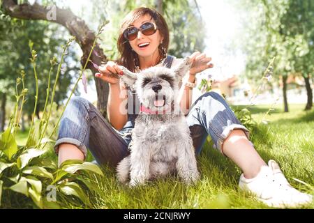Glückliche kaukasische Frau in Sonnenbrillen Ruhe in der Natur mit ihrem geliebten Hund schnauzer. Konzept der Liebe zu Tieren. Beste Freunde Stockfoto