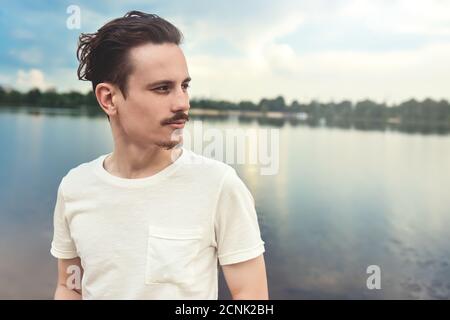 Portrait of Young man genießt eine schöne Aussicht und blickt in die Ferne in der Nähe eines Sees und Wald . Sommer . Frühling . Natur. Stockfoto
