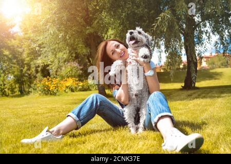 Hübsche Erwachsene kaukasische glückliche Frau, die sich an einem sonnigen Tag mit ihrem geliebten Hund im Park ausruhte. Weibchen liegt auf dem Gras, lächelnd an Stockfoto