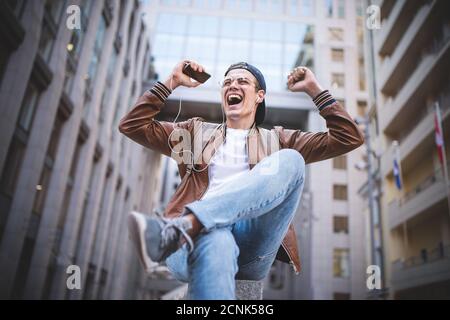 Fröhlicher Mann, der Musik mit Kopfhörern von einem Smartphone auf der Straße hört. Stockfoto