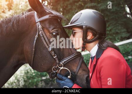 Ein junges Mädchen Jockey reden und küssen ihr Pferd. Sie liebt die Tiere und verbringt freudig ihre Zeit in ihrer Umgebung. Stockfoto