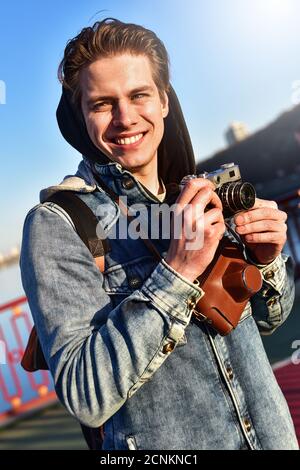 Junger fröhlicher Mann Fotograf, der mit der Kamera fotografiert Stockfoto