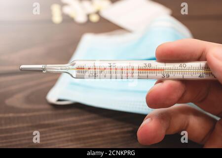 Ein medizinisches klinisches Quecksilberthermometer in der Hand, das die Temperatur von 39 C zeigt. Hohe Temperatur. Hölzerner Hintergrund. Th Stockfoto