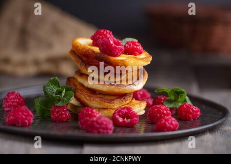 Hausgemachtes Frühstück oder Brunch: amerikanische Pfannkuchen mit Beeren und Zuckerpulver auf einem alten Schneidebrett mit einer Tasse schwarzem Tee Stockfoto