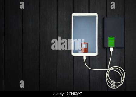 Powerbank lädt Tablet PC, Smartphone - isoliert auf Holzhintergrund. Ladekonzept. Freier Copyspace. Energie Stockfoto