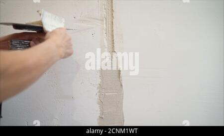 Dekorative Gipsbeschichtung. Der Mensch tut zerlumpte Textur an der Wand mit einem Spachtel. Gipsauftrag an der Wand Stockfoto