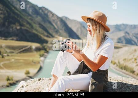 Schöne lächelnde blone junge Frau Reisende in Filzhut mit Fotokamera in den Händen, Reise in die Berge, Altai Stockfoto