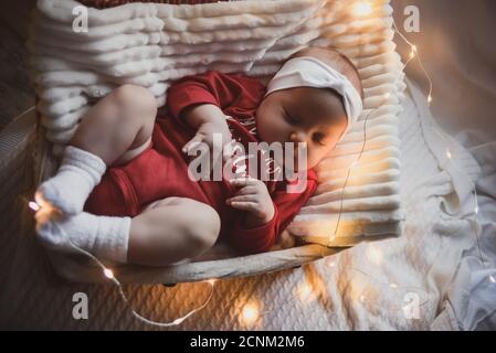 Kleine Rutschbaby mit weihnachtskleidung in Korb weihnachtsdekoration und Blitzlicht um sie herum. Stockfoto