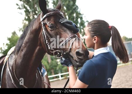 Nahaufnahme der Jockey Frau umarmt ein Pferd. Junges Mädchen streicheln ihr Pferd im Stall. Konzept der Pferdentherapie. Liebe zwischen Peo Stockfoto