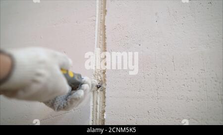Bauarbeiter mit langer Kelle, die eine Wand verputzt. Nahaufnahme von Beton. Arbeiter schließt Risse mit Mörtel an einer weißen Wand. Stockfoto